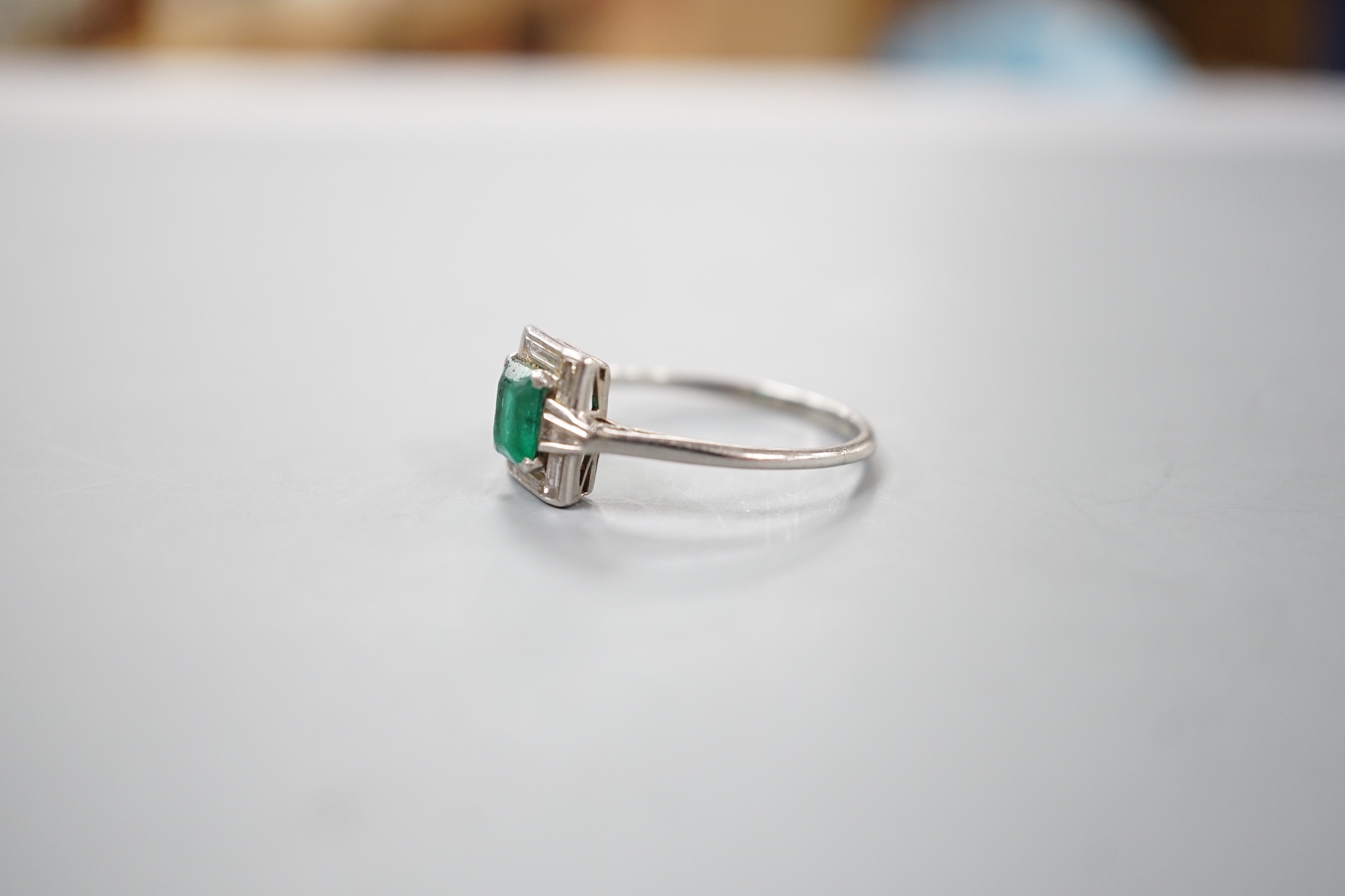 An Art Deco white metal, single stone emerald, baguette and trapeze cut diamond cluster set ring, size R/S, gross 3.5 grams